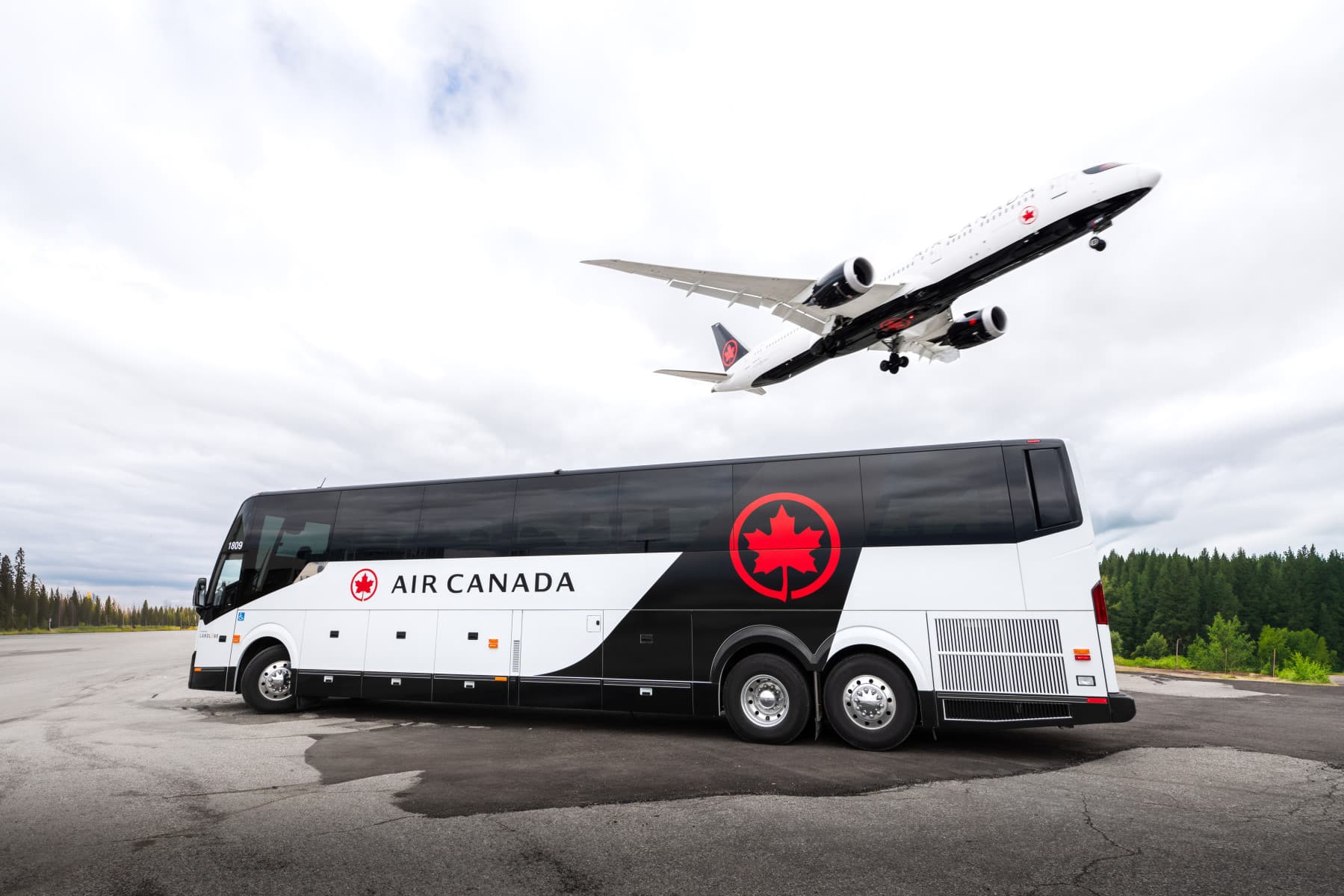 Air Canada shuttle on a tarmac with a plane from the same airline taking off above.