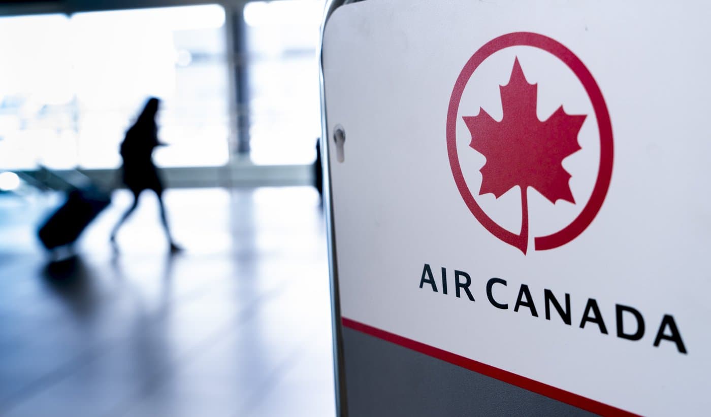 Logo Air Canada au premier plan avec une silhouette de voyageur floue dans un aéroport.