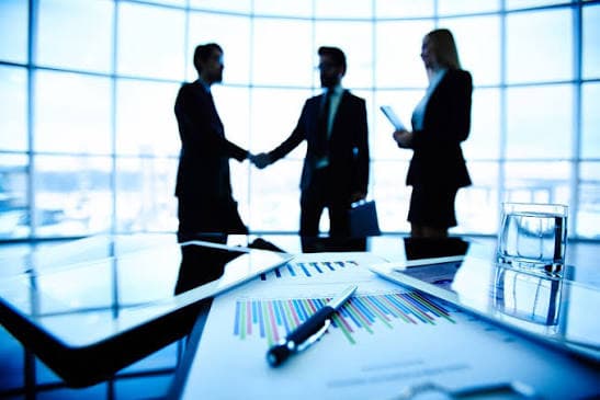 Silhouettes de professionnels se serrant la main avec des graphiques financiers au premier plan.