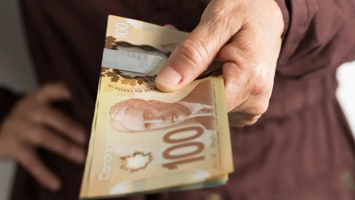 Main ridée tenant une liasse de billets de cent dollars canadiens de couleur marron.