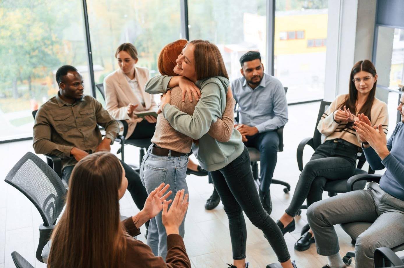 Deux femmes s'enlacent au milieu d'un groupe de soutien qui les applaudit.
